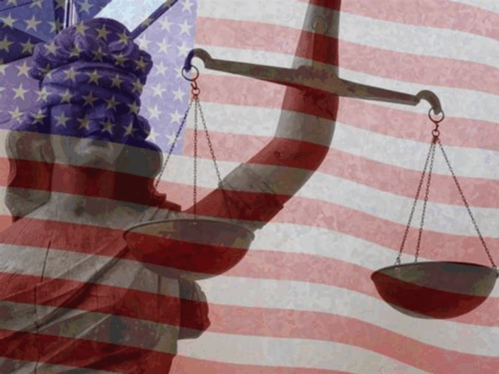 A translucent red, white, and blue American flag waves in the background behind a blindfolded Lady Justice holding scales.